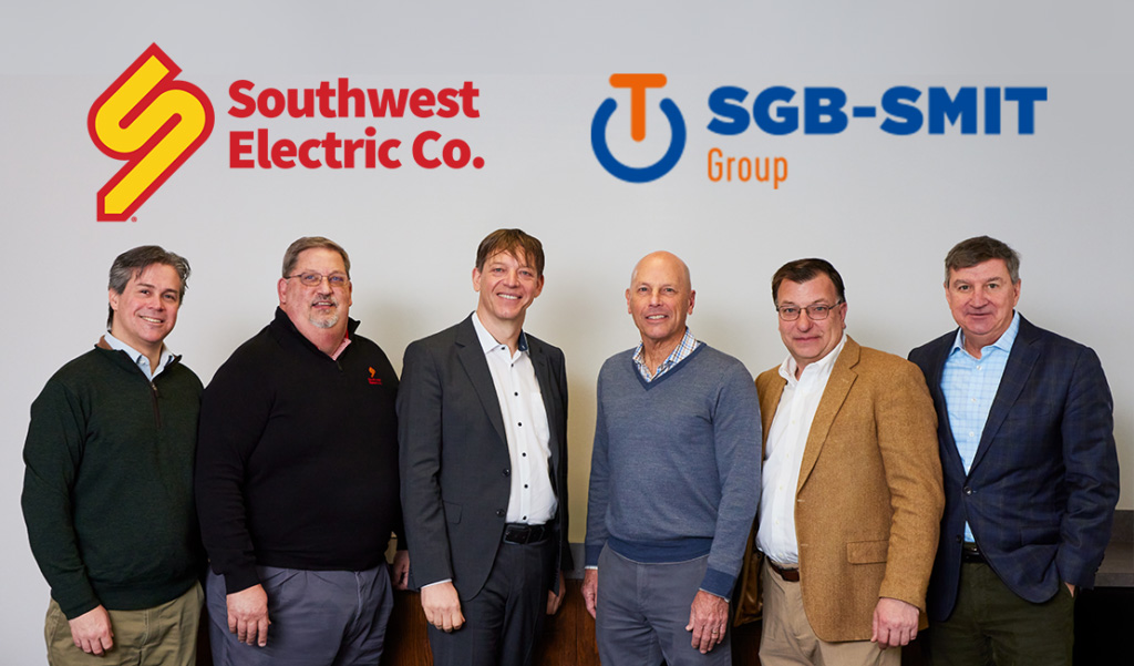 A group of business executives from Southwest Electric Co. and SGB-SMIT Group posing together in front of their company logos, highlighting a corporate partnership.